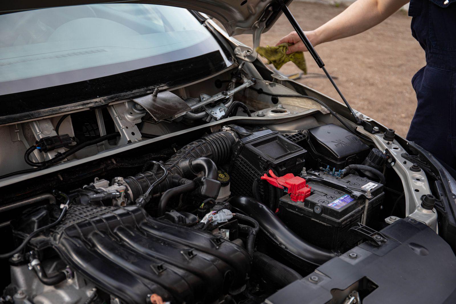 Open car hood showing the engine bay and 12-volt battery during an inspection