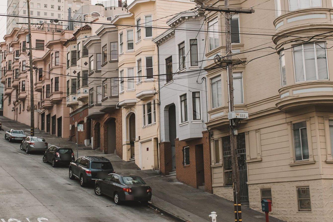 Cars parked with their wheels curbed along a steep San Francisco street lined with bay-window flats