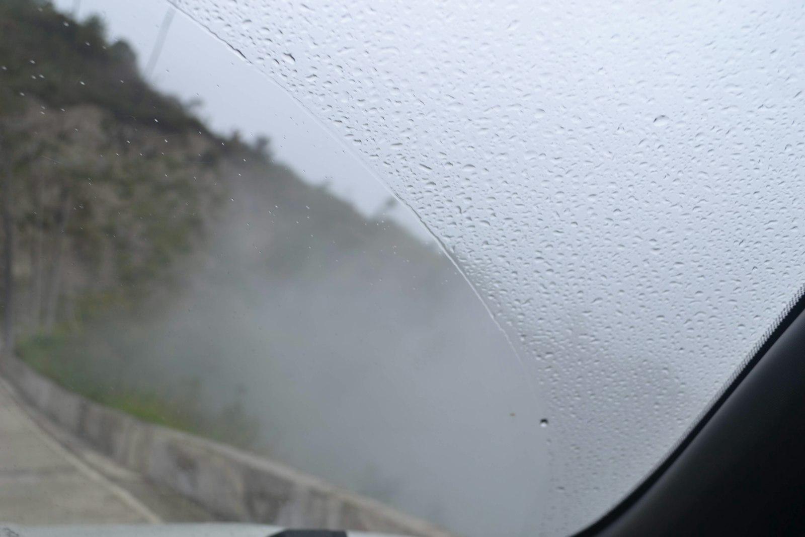 Fogged-up windshield seen from inside a car on a rainy day, blocking the view of the road