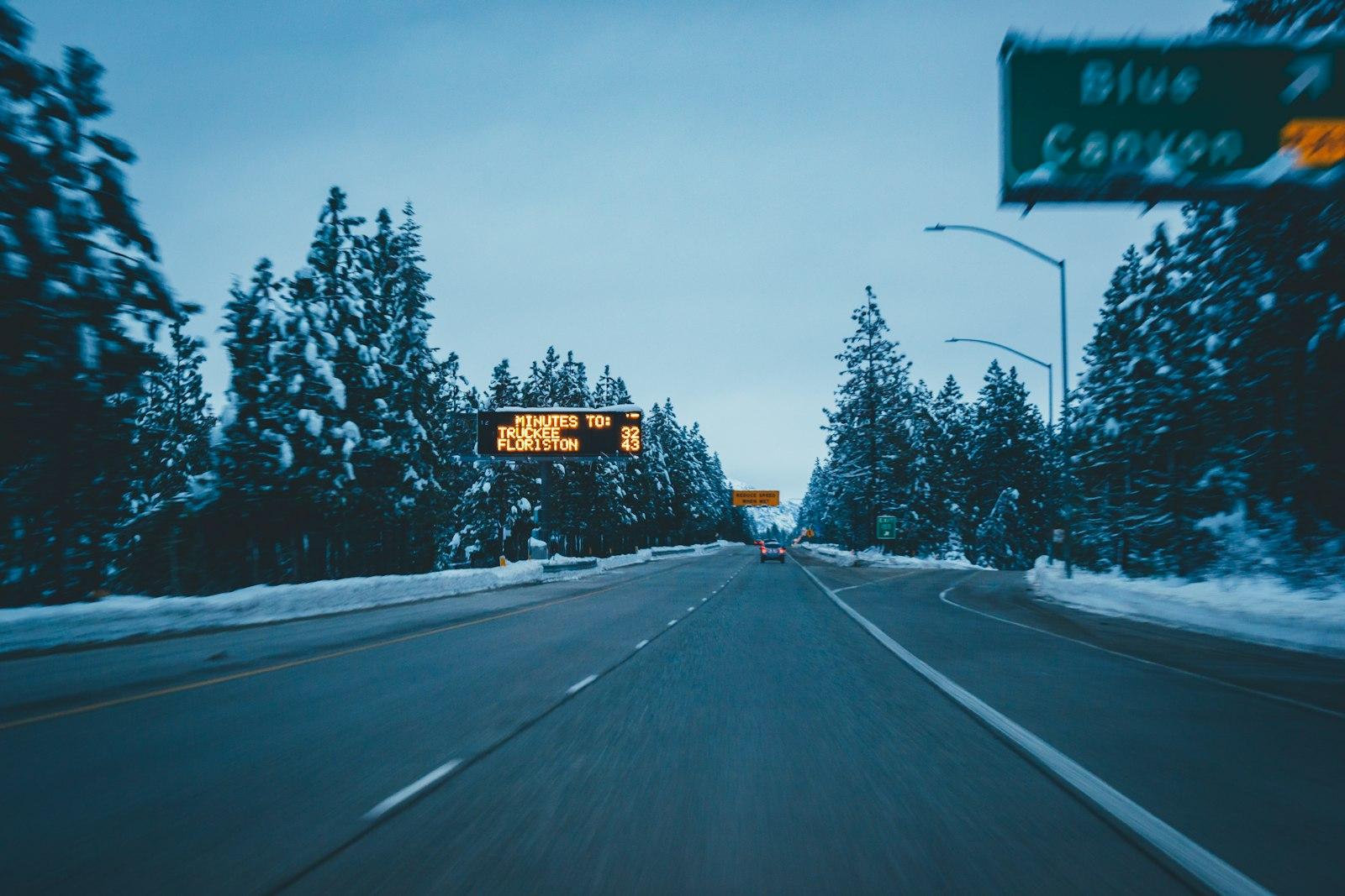 Interstate 80 near Blue Canyon in winter, with snowy pines and a travel-time sign to Truckee