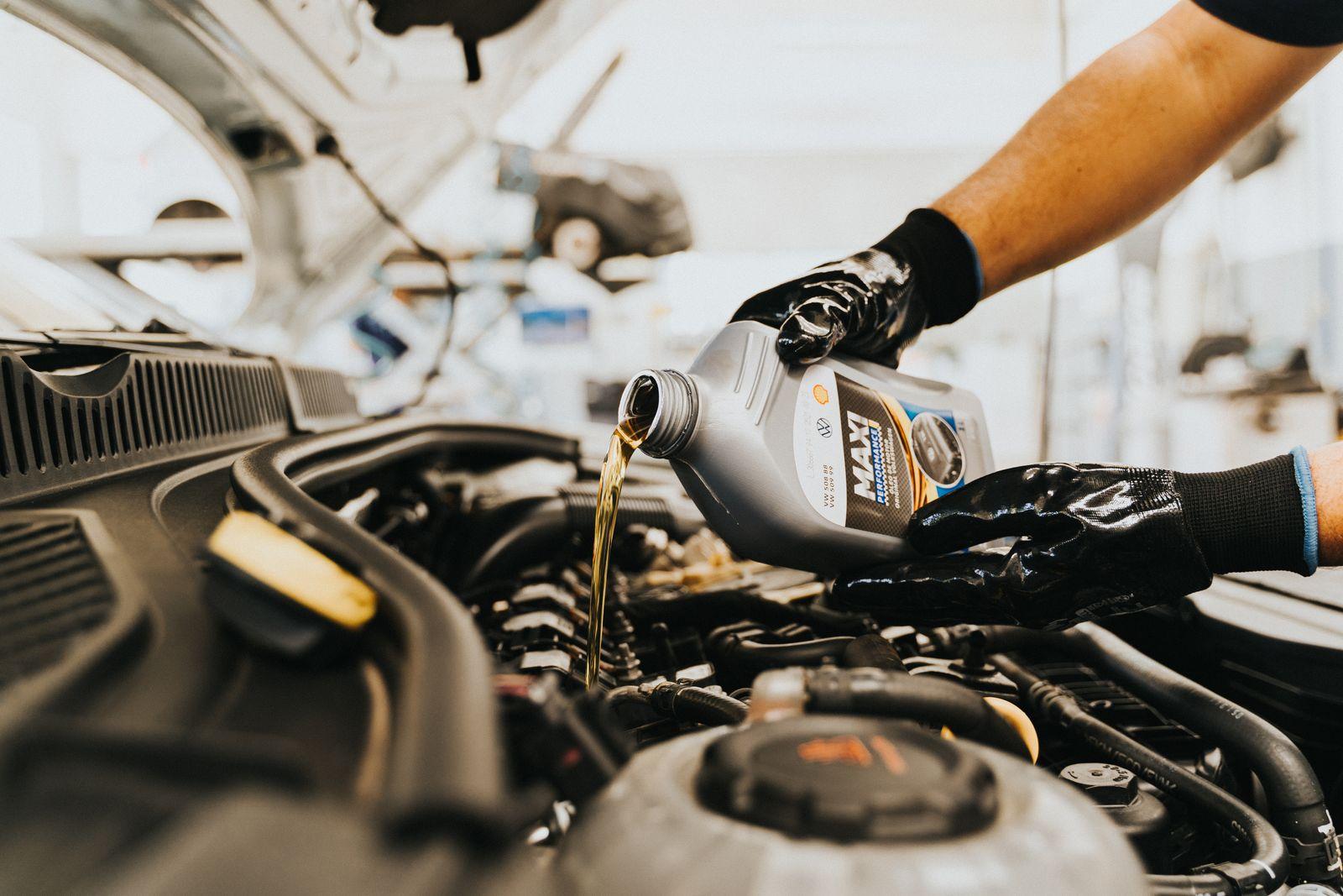 Mechanic in gloves pouring fresh motor oil into a car engine during an oil change