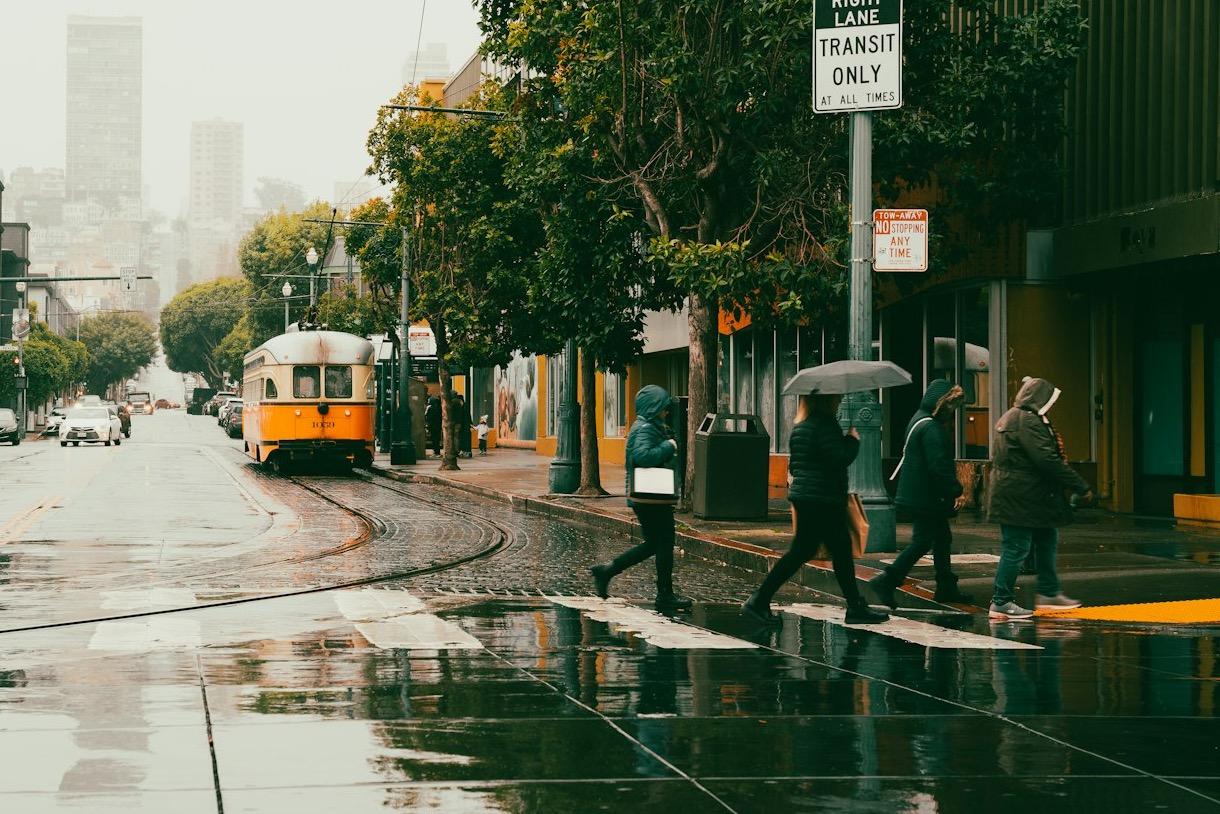 Rainy season in San Francisco: a Muni streetcar on wet rails as people cross a rain-soaked street