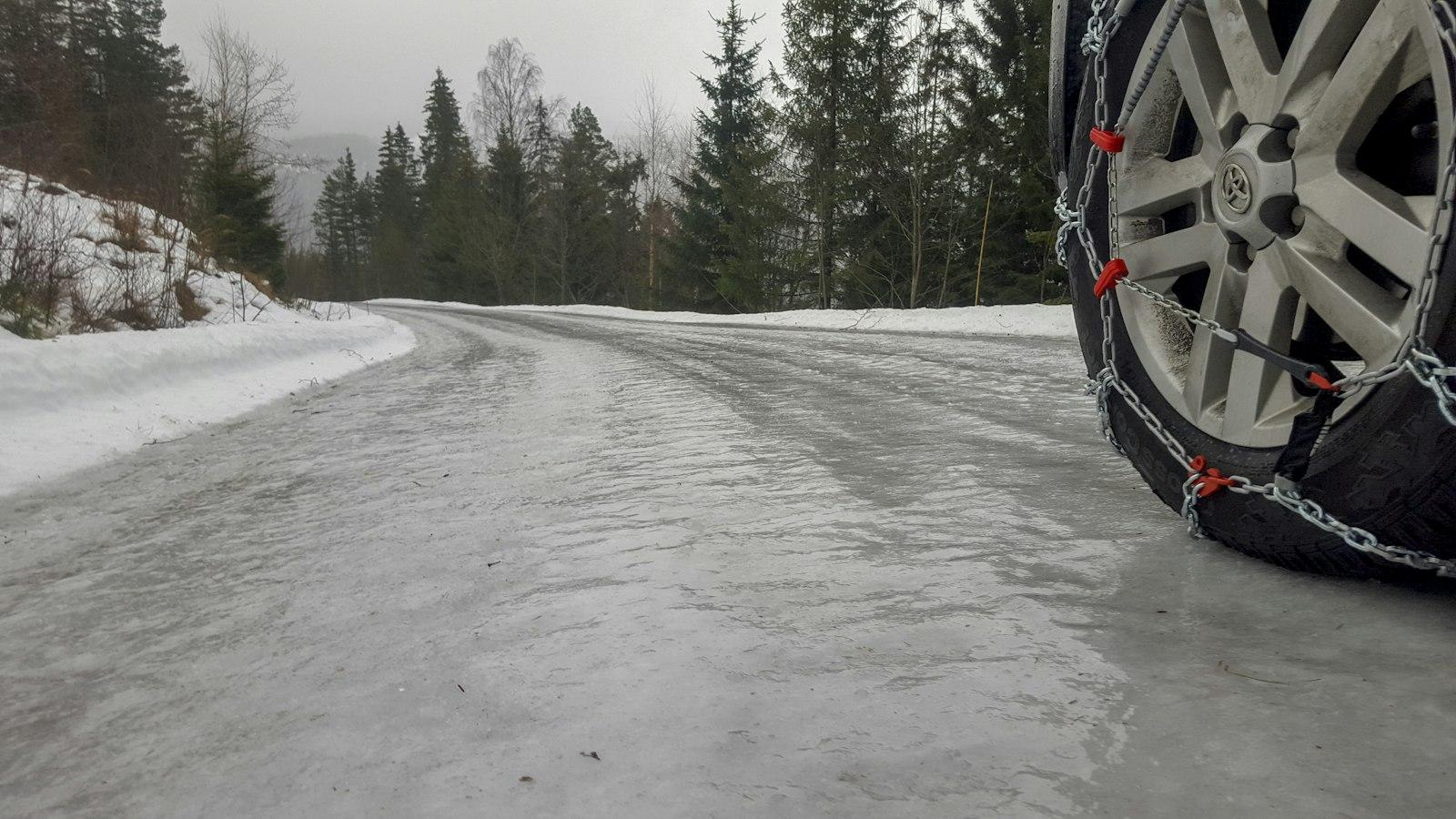 Tire chains fitted on a car wheel on an icy, snow-lined mountain road