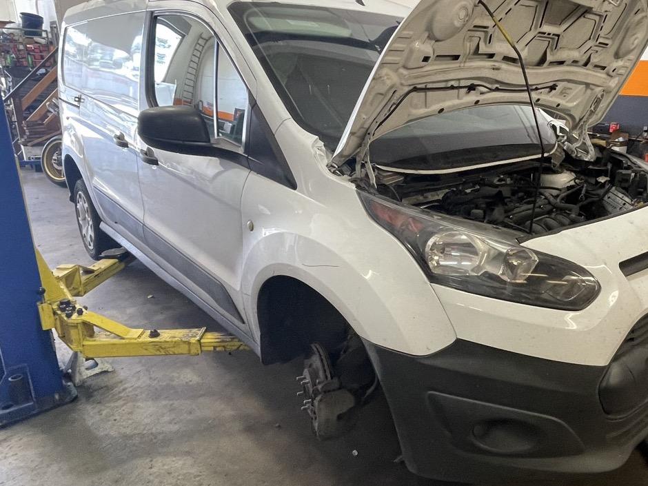 White van on a lift with the front wheel removed, exposing the brake caliper and rotor, at 415 Mechanix in Potrero Hill
