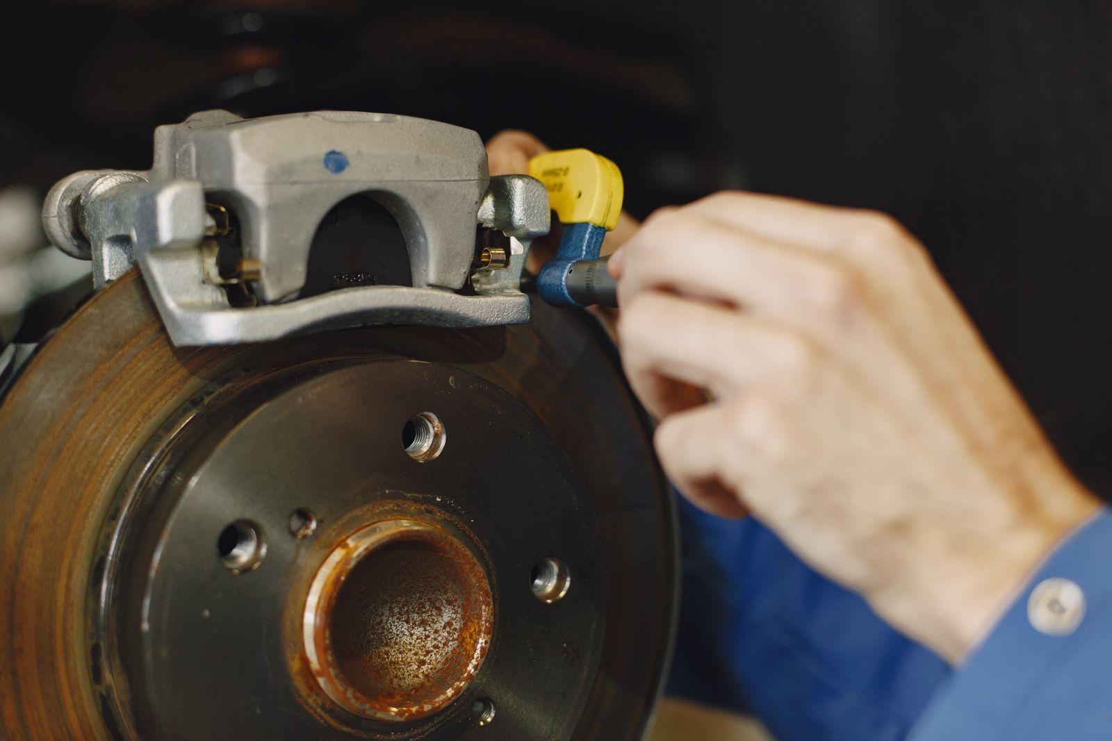 Mechanic measuring a brake rotor with a micrometer next to the caliper, with the wheel removed